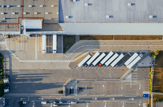 Aerial view of a concrete commercial warehouse with a large storage area and semi truck trailers.