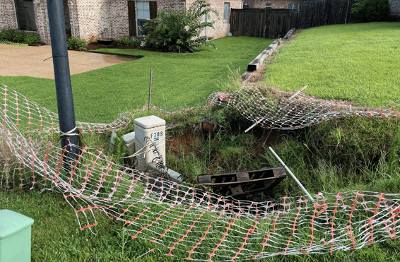Large sinkhole in a government property undergoing soil stabilization treatment to prevent further ground collapse.